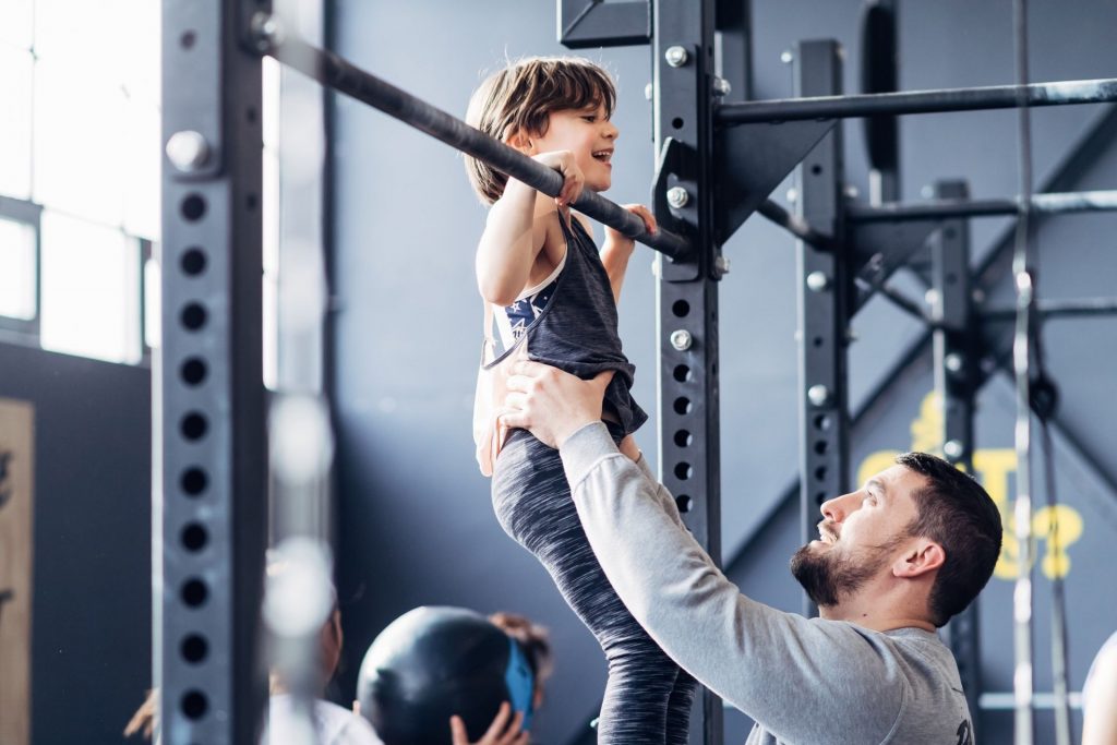 Father and daughter using pull up bar in gym